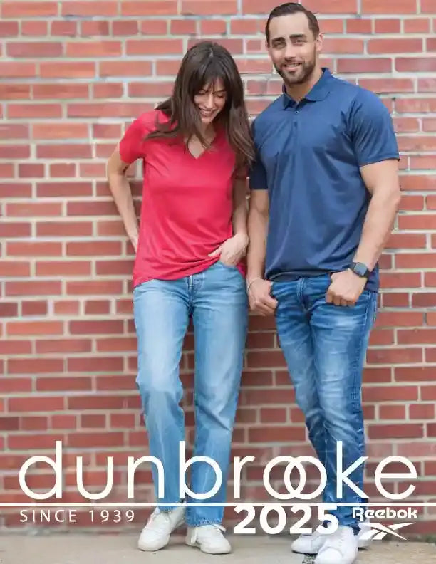 A man and a woman stand together against a brick wall, both wearing casual denim jeans.