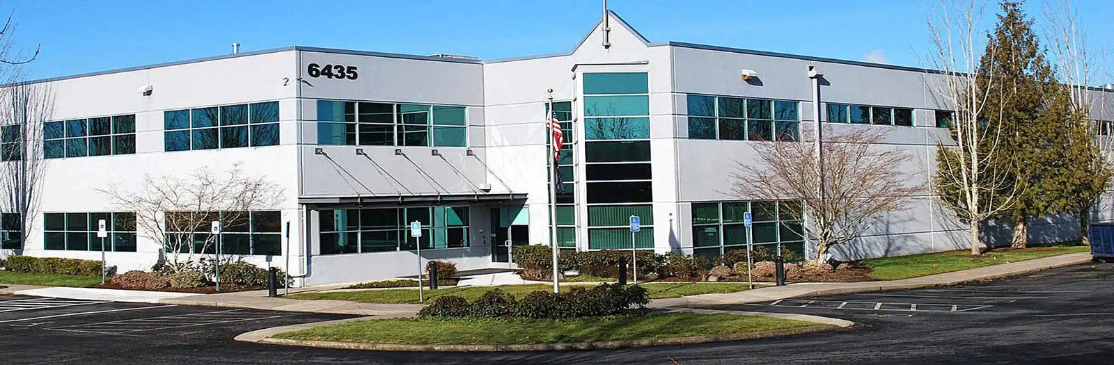 A modern office building with a mix of glass and solid facades, featuring multiple windows, a central entrance with an awning, and a flagpole.