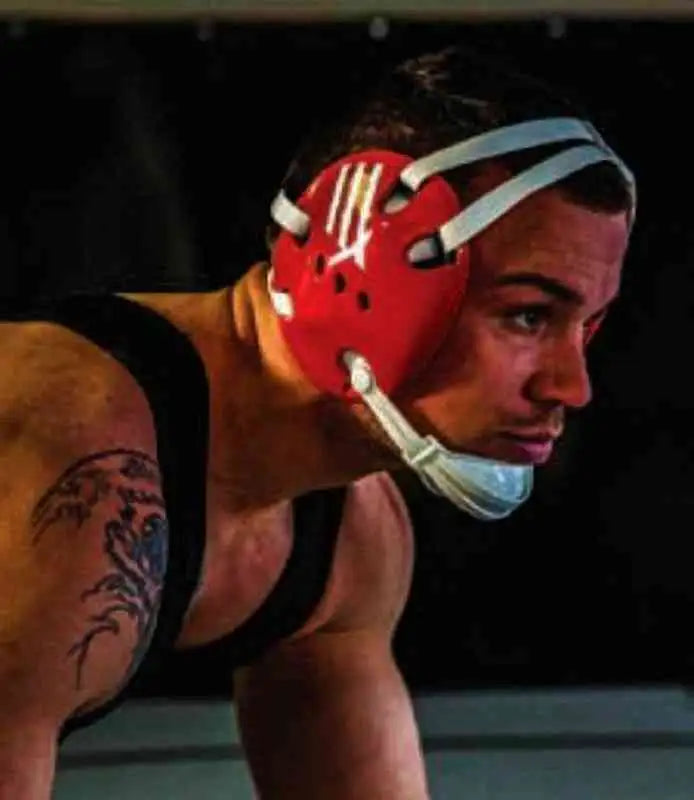 Red wrestling headgear with white straps and a stylized logo on the front.